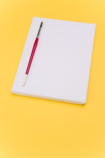 top view shot of blank white paint canvas and tools on a yellow paper surface with copy space
