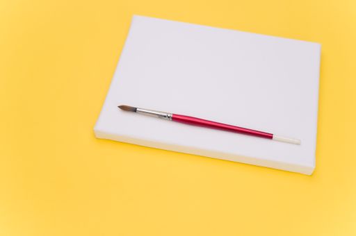 top view shot of blank white paint canvas and tools on a yellow paper surface with copy space