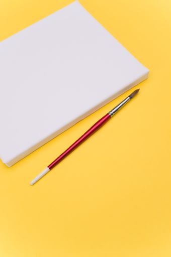 top view shot of blank white paint canvas and tools on a yellow paper surface with copy space