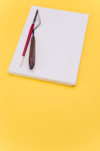 top view shot of blank white paint canvas and tools on a yellow paper surface with copy space