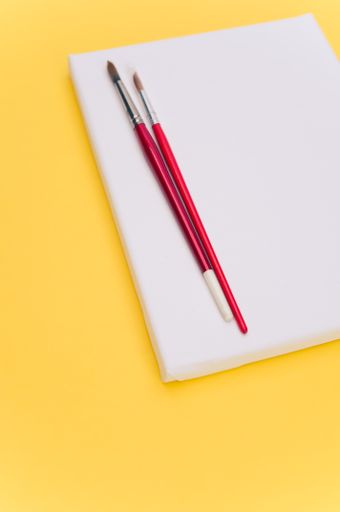 top view shot of blank white paint canvas and tools on a yellow paper surface with copy space