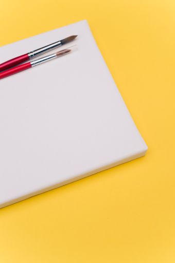 top view shot of blank white paint canvas and tools on a yellow paper surface with copy space