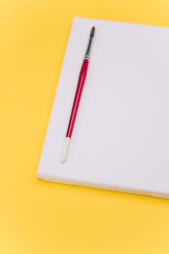 top view shot of blank white paint canvas and tools on a yellow paper surface with copy space