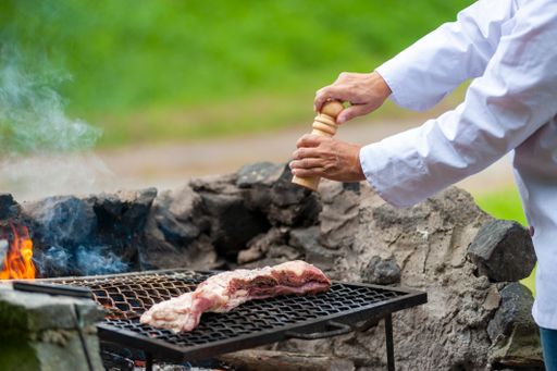 A chef pouring spices on barbecue on fire