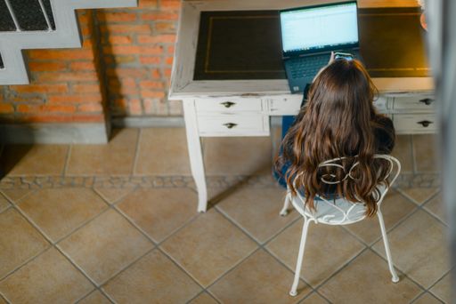 A top view of a young pretty woman in a sweater using a laptop and smartphone while sitting on a chair