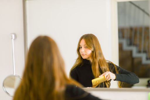 A close-up shot of a beautiful young caucasian girl combing hair looking at the mirror