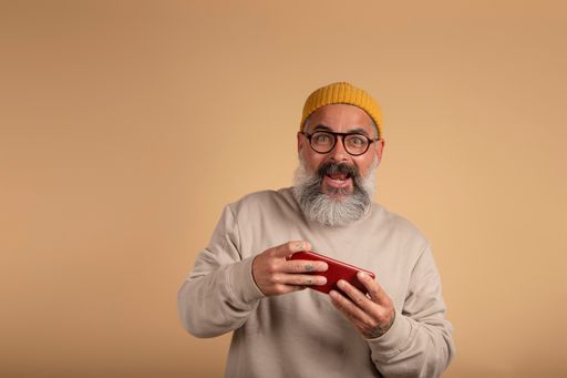 A handsome Spanish man with a white beard and yellow hat playing with a red smartphone