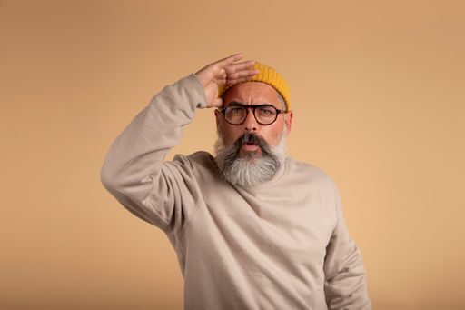 A Spanish man with a white beard and yellow hat looking far away with his hand on his forehead