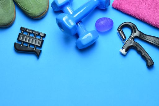 A top view of fitness tools. The dumbbells, hand and finger grips, balls, towel, and boots isolated on blue background