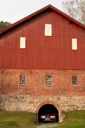 A vertical shot of an old red traditional Norwegianbarn used as a garage by an old Volvo car