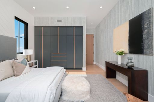 Modern bedroom interior with stylish furniture, a large wardrobe, and abstract art on the wall, featuring neutral tones and natural light.