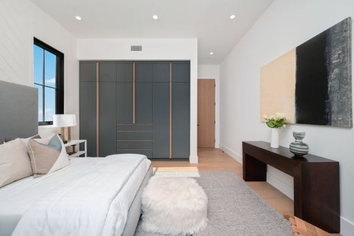 Modern bedroom interior with sleek furniture, a cozy bed, and minimalist decor, featuring a large wardrobe and abstract art.