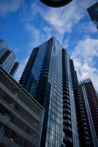 A vertical low angle closeup of high glass buildings at the city under a blue cloudy sky