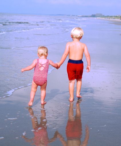 A boy holding hand of her sister and walking on the beach