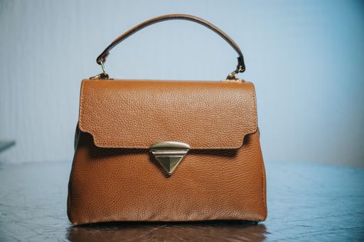 A closeup of a small brown handbag with a gold buckle