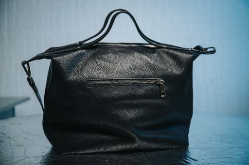 A closeup of a black leather handbag with thin straps on it and a zipper