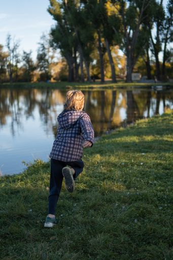 A blonde kid running on the riverside in spring