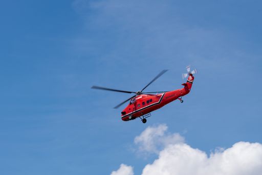 A flying red rescue helicopter against a clear blue sky