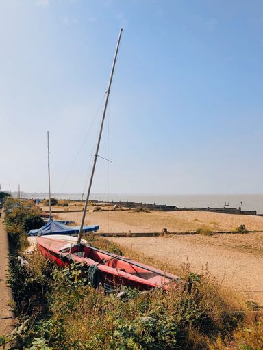 A vertical shot of an abandoned boat near the dried meadow in Whitstable, UK