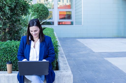 Beautiful Caucasian businesswoman with laptop and cup of coffee sitting outside working in the street, copy space