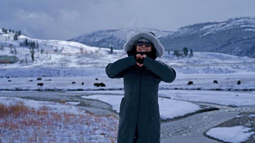 A young tourist female holding a heart with her hands posing near the snowy Yellowstone National Park