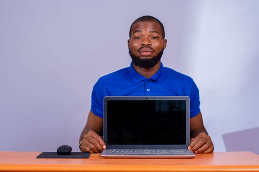 A young African male sitting at the office desk and showing his laptop screen