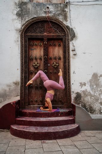 A young Caucasian woman doing yoga poses on a mat next to ancient wooden doors