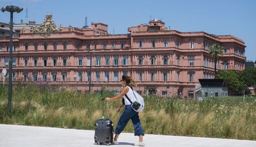 A female tourist walks in front of an old building with a suitcase in her hand in  Buenos Aires, Argentina