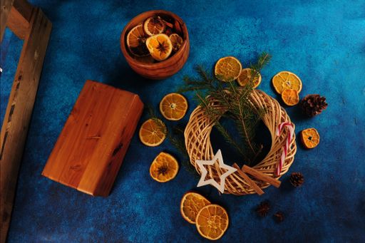 A close-up shot of a Christmas wreath with cinnamon sticks, pine twigs,c and orange slices, and a wooden box