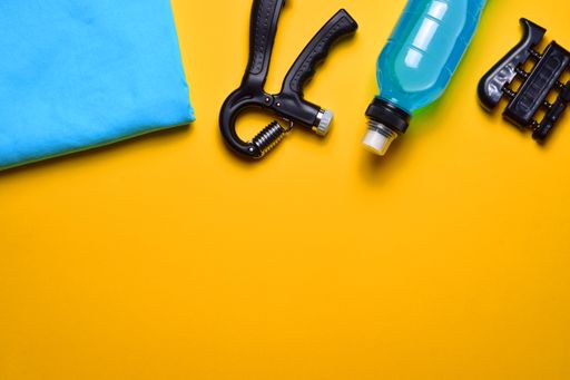 A top view of fitness tools. The water bottle, hand and finger grips, and towel isolated on orange background