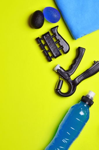 A vertical shot of fitness tools. The bottle, hand and finger grips, balls and towel isolated on a yellow background