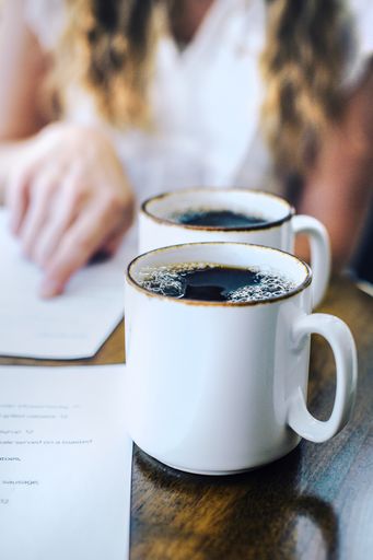 A vertical closeup of two coffee mugs on a wooden table with a blurred background