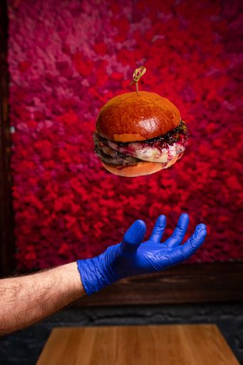 Fresh tasty burger above a male hand in a blue latex glove