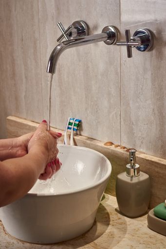 A vertical closeup of a female washing her hands in a bathroom under the lights