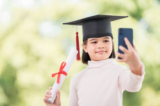 A happy Southeast Asian schoolgirl with a certificate and smartphone during graduation in Thailand