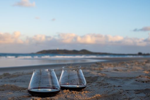 A closeup of two wine glasses placed together on the sand at the beach