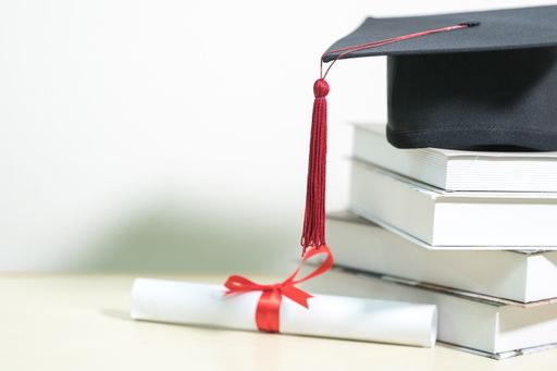 A closeup of a mortarboard and degree certificate on a white table, perfect for education concepts