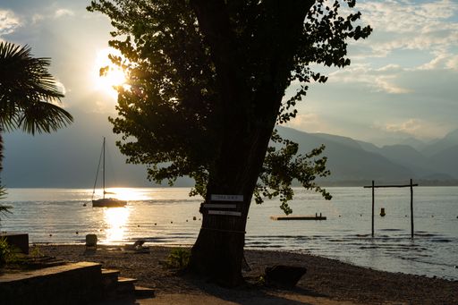 A beautiful view of a boat in a sea surrounded by trees and mountains at sunset