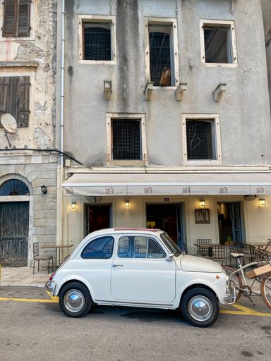 A Fiat 500 classic small car parked on a Corfu street with classic old style and architecture