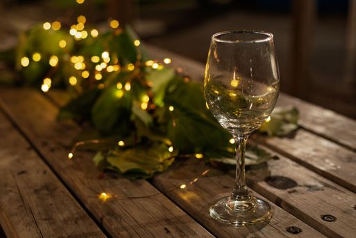 A wine glass on a rustic wooden table adorned with soft fairy lights and green leaves, creating a warm, cozy atmosphere.