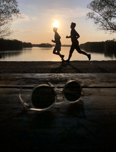 A closeup selective focus shot of sunglasses on two running humans silhouettes background