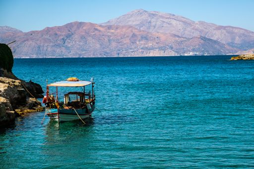 A small fishing boat in clear sea parked near the rocky shore and mountains in the background