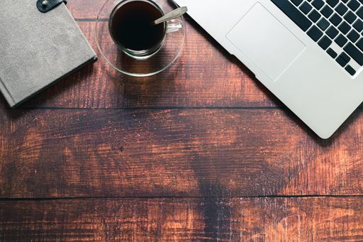 A closeup of the coffee mug, laptop, and book on the desk.
