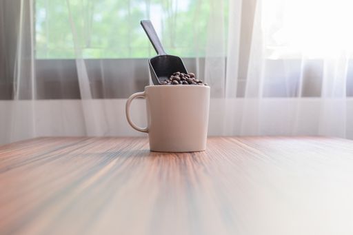 A mug with coffee beans and with a scoop on a wooden table behind the window