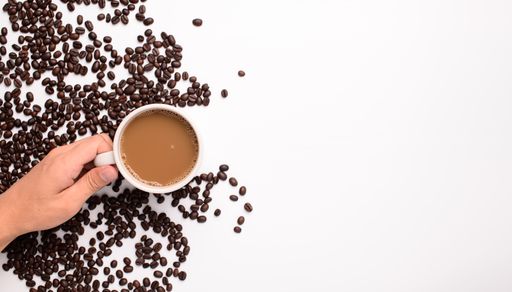 A top view of a coffee mug with coffee and beans on a white background with copy space
