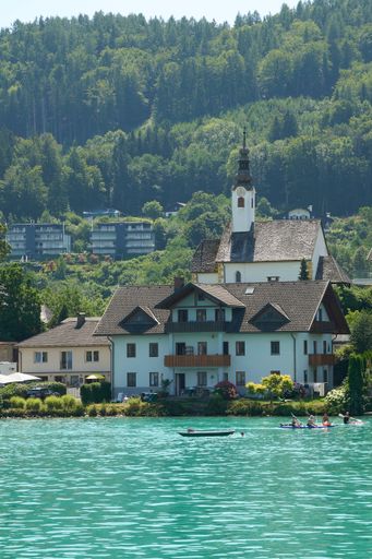 A stunning aerial view of a beautiful house, situated by a tranquil lake surrounded by lush green forests in the Carinthia region of Austria