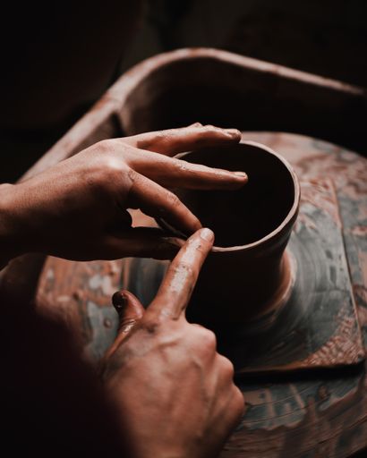 A person's hands and fingers crafting a clay pot