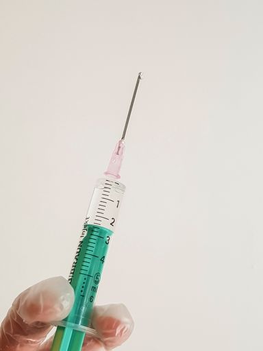 A vertical shot of a hand with a glove holding a syringe filled with liquid