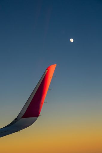 A vertical shot of the wing of an airplane during the flight at sunset