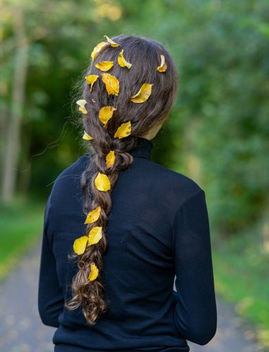 A back shot of a girl wearing a black with autumn leaves on her braids hair in the garden